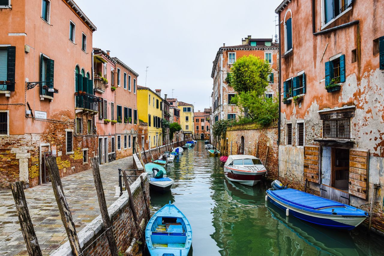 services-03 Picturesque view of a canal in Venice with moored boats and vibrant buildings.