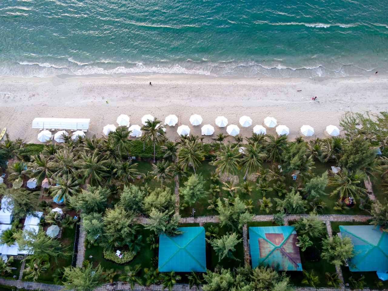about-us Stunning aerial shot of a tropical beach with white umbrellas and lush greenery.